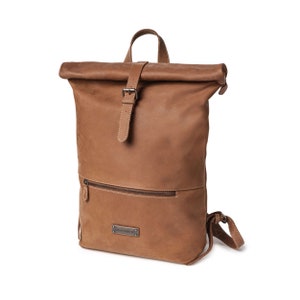May include: A brown leather backpack with a roll-top closure and a buckle. The backpack has a front pocket with a zipper and a small leather patch with the brand name "CRAFTHOLIC" on it.