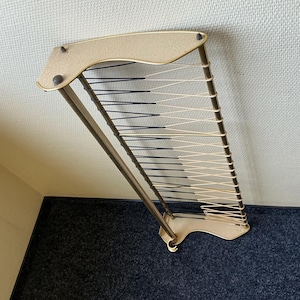 Può includere: Un attaccapanni vintage da parete con una cornice beige e una griglia di cordoncini neri e color crema. L'attaccapanni ha una parte superiore curva e una base decorativa, ideale per ingressi o camere da letto.