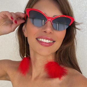 May include: Red cat-eye sunglasses with a gold trim and red feather earrings.