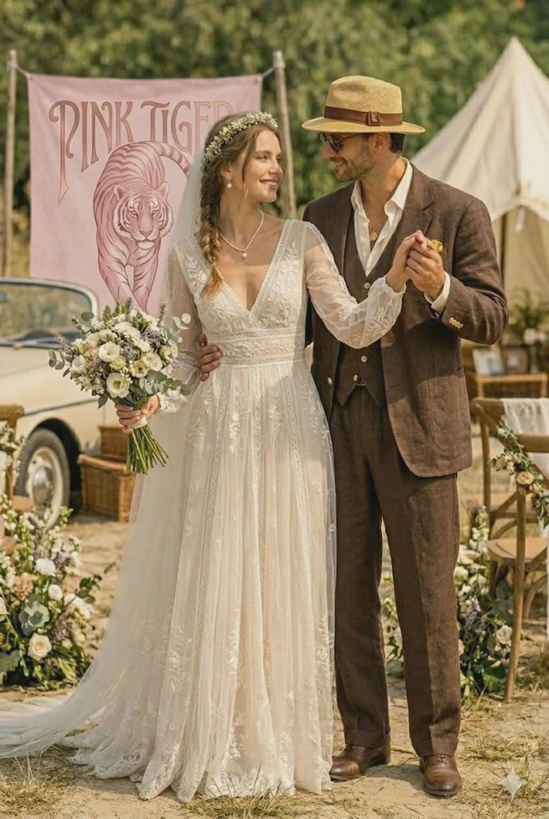 Puede incluir: Una pareja en una boda al aire libre. La novia lleva un vestido de novia de encaje blanco con mangas largas y una corona de flores. El novio lleva un traje marr&oacute;n y sombrero. Una pancarta con "PINK TIGER" y un tigre en el fondo.