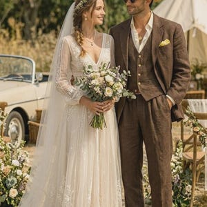 Puede incluir: Una pareja vestida para una boda al aire libre. La persona de la izquierda lleva un vestido de novia de encaje blanco con velo largo y sostiene un ramo. La persona de la derecha lleva un traje y sombrero marrones. Un coche antiguo y una tienda de campa&ntilde;a est&aacute;n al fondo.
