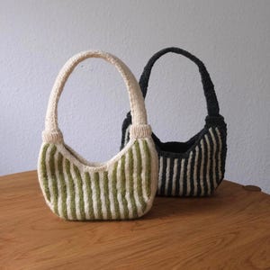 Può includere: Due borse a mano lavorate a maglia con manici ad arco sono appoggiate su una superficie di legno. Una borsa è a righe crema e verdi, l'altra a righe nere e crema. Le borse hanno una forma arrotondata e sono realizzate con filato strutturato.
