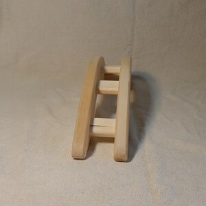 Puede incluir: Un arco de madera con tres listones horizontales, dise&ntilde;ado para que los animales peque&ntilde;os puedan trepar por encima. El arco est&aacute; hecho de madera natural y tiene un color marr&oacute;n claro.