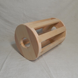 May include: A wooden cylinder with a series of slats running lengthwise. The cylinder has a large hole on one side and a smaller hole on the other side.