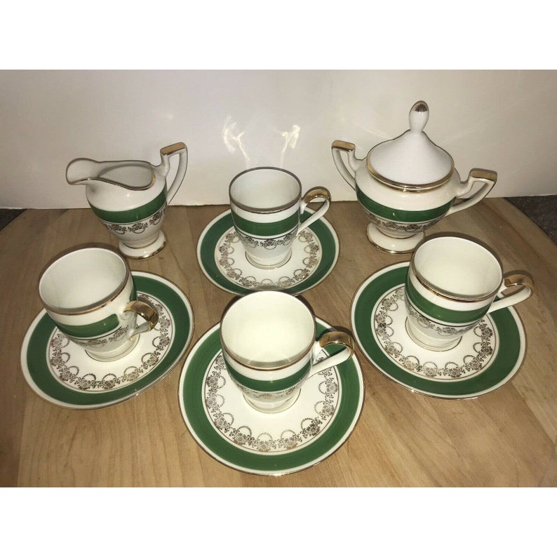 Puede incluir: Un juego de tazas de t&eacute; y platillos verdes y dorados con una jarra de crema y un azucarero a juego. Las tazas y los platillos tienen un dise&ntilde;o floral verde y dorado.