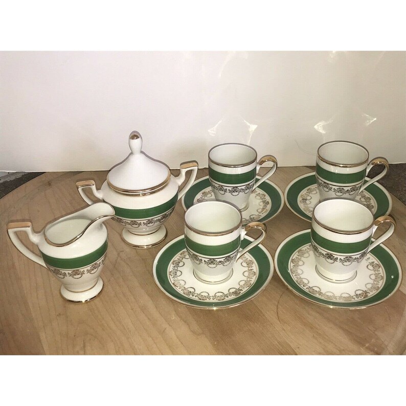 Puede incluir: Un juego de t&eacute; blanco con ribetes verdes y dorados. El juego incluye una jarra de crema, un azucarero y cuatro tazas y platillos.