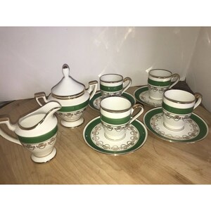 Puede incluir: Un juego de t&eacute; blanco con ribetes verdes y dorados. El juego incluye una jarra de crema, un azucarero y cuatro tazas y platillos.