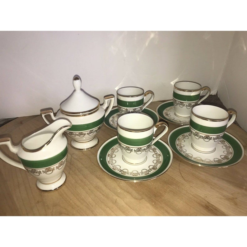 Puede incluir: Un juego de t&eacute; blanco con ribetes verdes y dorados. El juego incluye una jarra de crema, un azucarero y cuatro tazas y platillos.