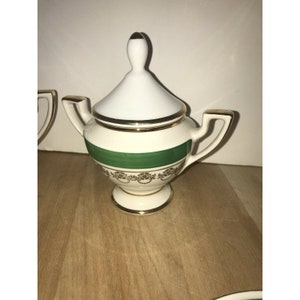 Puede incluir: Azucarero de porcelana blanca con una banda verde y ribete dorado. La tapa tiene un pomo en la parte superior.