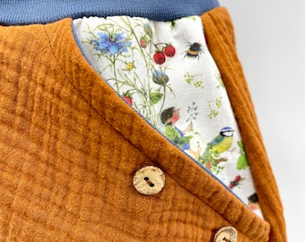May include: Brown corduroy pants with a floral print pocket and two brown buttons. The pants have a blue waistband.