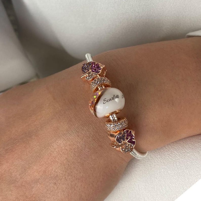 breast milk jewelry bracelet with 16x10mm breastmilk bead including half diagonal section of rose gold and opal flakes and other half with breastmilk and child name, separated by a lock of hair with rose gold cores from KeepsakeMom
