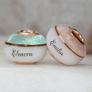 breastmilk jewelry bead with half birth color and opal flakes, half milk with child name, and lock of hair in the middle to separate with rose gold plated sterling silver cores from KeepsakeMom