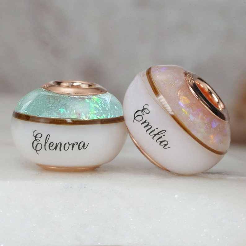 breastmilk jewelry bead with half birth color and opal flakes, half milk with child name, and lock of hair in the middle to separate with rose gold plated sterling silver cores from KeepsakeMom