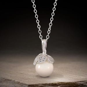 May include: A silver necklace with a white pearl pendant. The pendant is adorned with small silver leaves and clear cubic zirconia stones.