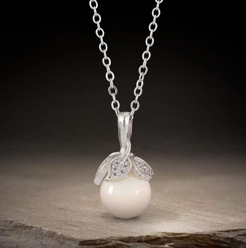 May include: A silver necklace with a white pearl pendant. The pendant is adorned with small silver leaves and clear cubic zirconia stones.