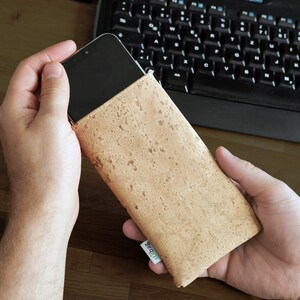Puede incluir: Una funda de tel&eacute;fono de corcho marr&oacute;n con un logotipo verde "Slubber". La funda est&aacute; hecha de corcho natural y tiene una superficie texturizada.
