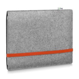 May include: A rectangular light gray felt laptop sleeve featuring a vibrant orange elastic band wrapped horizontally around the center to secure the contents. A small white fabric tag with the text stilbag is attached to the top edge.