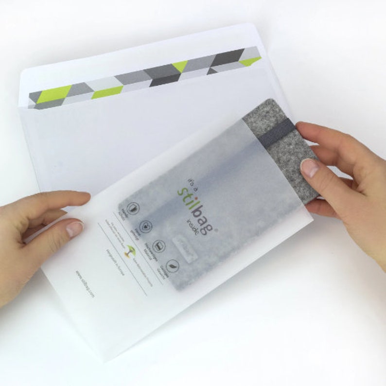 May include: A white envelope with a green and gray geometric pattern on the front. The envelope is open and a gray felt phone case is being pulled out. The phone case has the text "it's a stilbag inside" printed on it.