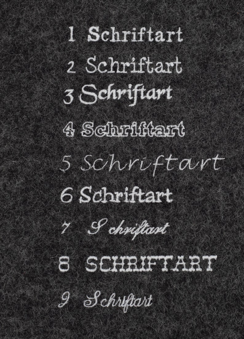 May include: A close-up of a black textured surface with nine examples of the word "Schriftart" written in different fonts and styles.