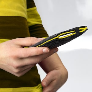 Könnte beinhalten: Eine schwarze Handyhülle aus Filz mit gelbem Rand und einem schwarzen Gummiband.