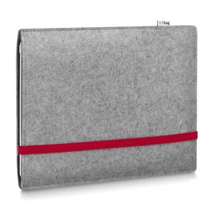 May include: A rectangular light gray felt sleeve for a tablet or laptop, featuring a horizontal bright red elastic band across the front and a small white fabric tag with the text stilbag attached to the top edge of the gray felt material.