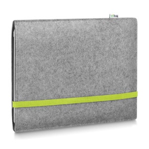 May include: A rectangular gray felt sleeve for a tablet or laptop, featuring a bright lime green elastic band wrapped horizontally around the center to secure the closure. A small white fabric tag with the text stilbag is attached to the top edge.