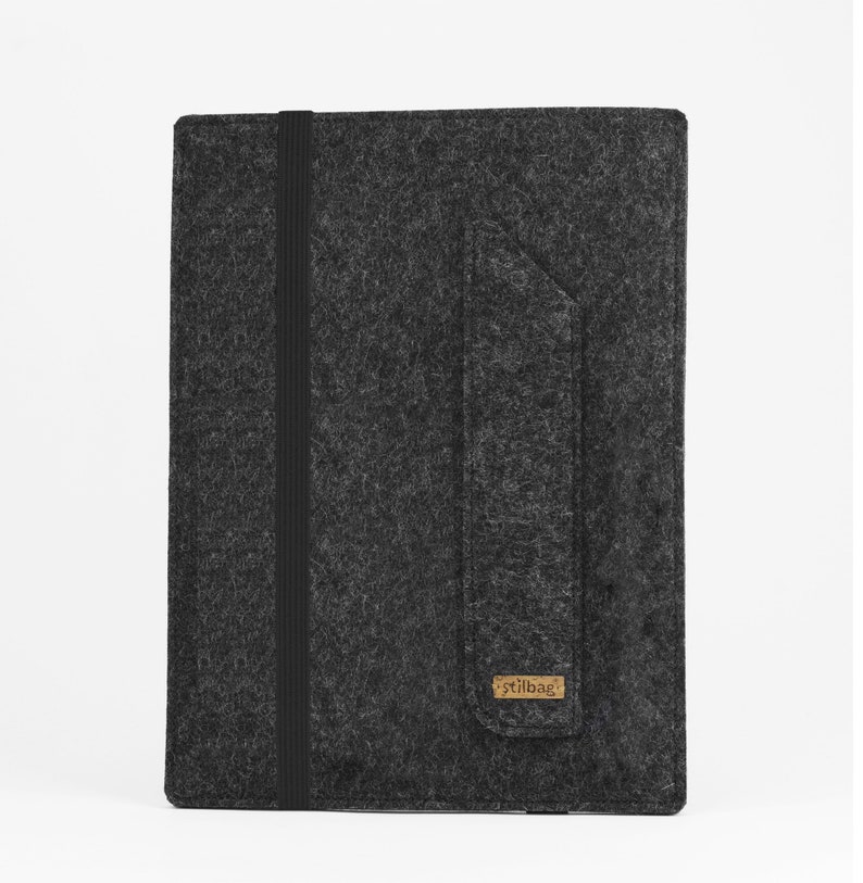 May include: A dark gray felt sleeve for a tablet or notebook, featuring a vertical black elastic band closure and a side pocket flap. A small rectangular brown label with the text stilbag is attached to the bottom corner of the pocket.