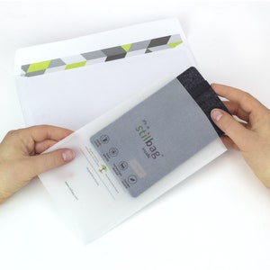 May include: A white envelope with a green and gray geometric pattern on the front. The envelope is open and a gray felt pouch is inside. The pouch has the text "It's a Stilbag inside" printed on it.