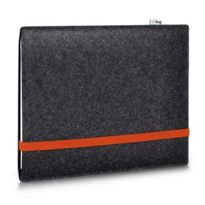 May include: A dark gray felt laptop sleeve featuring a vibrant orange elastic band wrapped horizontally around the center. A small white fabric tag with the text stilbag is attached to the top edge of the rectangular protective case.