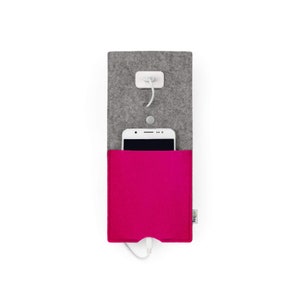 May include: A grey felt phone charging pouch with a pink felt pocket inside. A white smartphone is in the pocket and a white charging cable is plugged into the phone and the wall adapter.