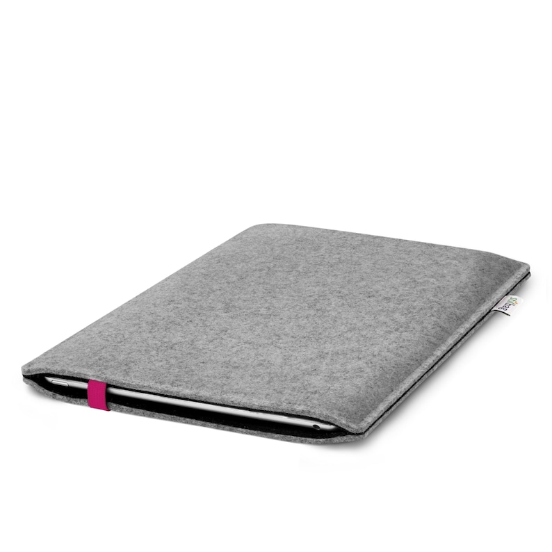 May include: A light gray felt laptop sleeve with a black interior lining. The sleeve features a bright pink elastic band closure on the side and a small white fabric tag with black text on the right edge, holding a thin silver electronic device.