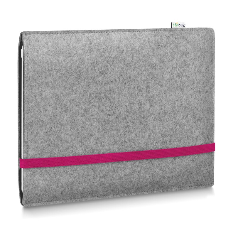 May include: A rectangular gray felt sleeve for a tablet or laptop, featuring a vibrant hot pink elastic band wrapped horizontally around the center to secure the closure. A small white fabric tag with the text stilbag is attached to the top edge.