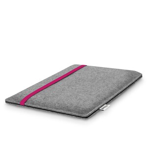 May include: A rectangular gray felt laptop sleeve featuring a vibrant magenta elastic band stretched across the front cover. The sleeve has a slim profile with black edge detailing and a small white fabric tag with black text on the side.