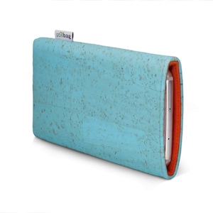 Op de afbeelding: Een turquoise kurken telefoonhoesje met een oranje binnenkant. De hoes heeft een rechthoekige vorm en een textuur. De merknaam "stilbag" staat op een klein label.