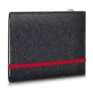 May include: A dark gray rectangular felt sleeve for a laptop or tablet, featuring a horizontal bright red elastic band across the front and a small white fabric tag with the text stilbag attached to the top edge of the case.