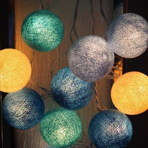 Könnte beinhalten: Eine Lichterkette aus Baumwollkugeln in verschiedenen Farben, darunter Blau, Grün und Gelb. Die Lichter sind mit einem durchsichtigen Draht verbunden und eignen sich perfekt, um jedem Raum eine Prise Verspieltheit zu verleihen.