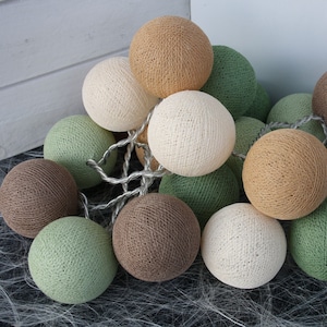 Könnte beinhalten: Eine Lichterkette aus Baumwollkugeln in verschiedenen Farben, darunter Braun, Beige, Grün und Weiß. Die Lichter sind mit einem silbernen Draht verbunden.