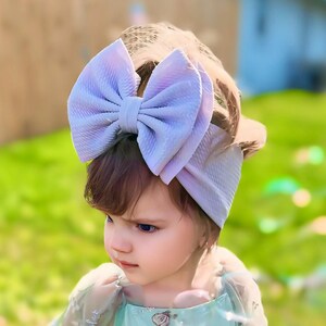May include: A young girl wearing a light green dress with floral embroidery and a large lavender bow headband. The dress has sheer sleeves and a tulle skirt.