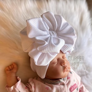 May include: A white baby bow headband with a large, fluffy bow. The headband is made of soft, stretchy fabric and is perfect for newborns and infants.
