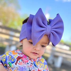 May include: A young child wearing a purple bow headband and a white t-shirt with a cartoon print. The shirt features characters from the Nickelodeon show "The Fairly OddParents".