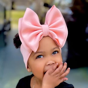 May include: A young child wearing a black shirt with the word "Mama" on it. The child is wearing a pink satin bow headband.