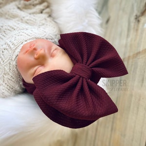 May include: A burgundy bow headband with a large bow. The headband is made of a soft, stretchy material and is perfect for newborns and babies.