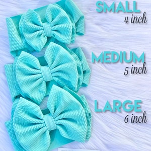 May include: Three turquoise fabric headbands with bows of varying sizes. The bows are 4 inches, 5 inches, and 6 inches wide. The text "SMALL 4 inch", "MEDIUM 5 inch", and "LARGE 6 inch" is written in white text on a white background.