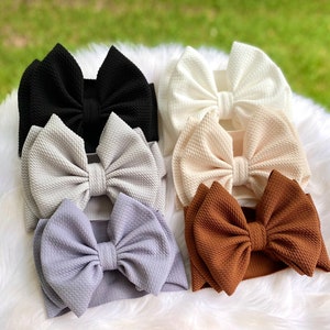 May include: A set of eight fabric headbands with large, knotted bows in various colors, including black, white, brown, and gray.