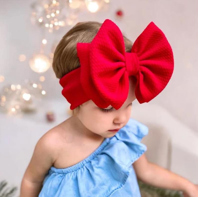 May include: A red fabric headband with a large, oversized bow. The headband is worn by a young child.