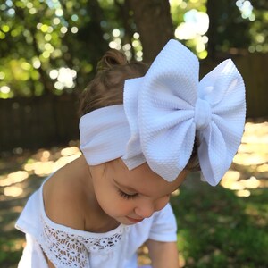 May include: A white ceramic mug with a black handle and the text "But First, Coffee" in a bold, black font. The mug is set against a blurred background, suggesting a cozy setting.