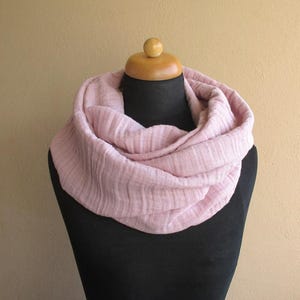 Könnte beinhalten: Hellrosa Infinity-Schal aus weichem, strukturiertem Stoff. Der Schal ist um eine schwarze Schaufensterpuppe drapiert und zeigt sein kreisförmiges Design. Der Hintergrund ist einfarbig beige.