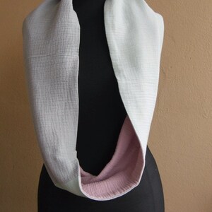 May include: A light gray infinity scarf with a pink lining. The scarf is displayed on a black mannequin.