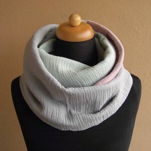 May include: A soft, gray infinity scarf with a pink and light green ombre effect. The scarf is made of a textured fabric and is folded in a loop.