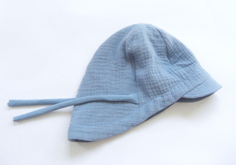 May include: A light blue sun hat with a wide brim and a tie string. The hat is made of a soft, textured fabric.